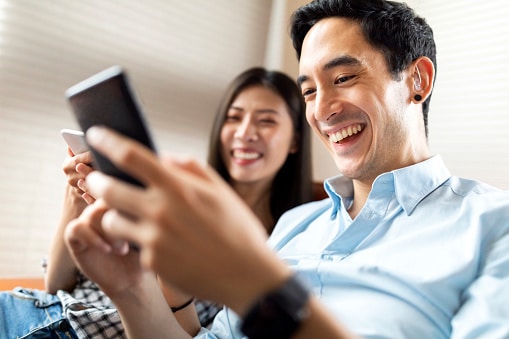 Joys of a newly repaired hearing aid Man and woman on a couch looking at their cell phones and smiling